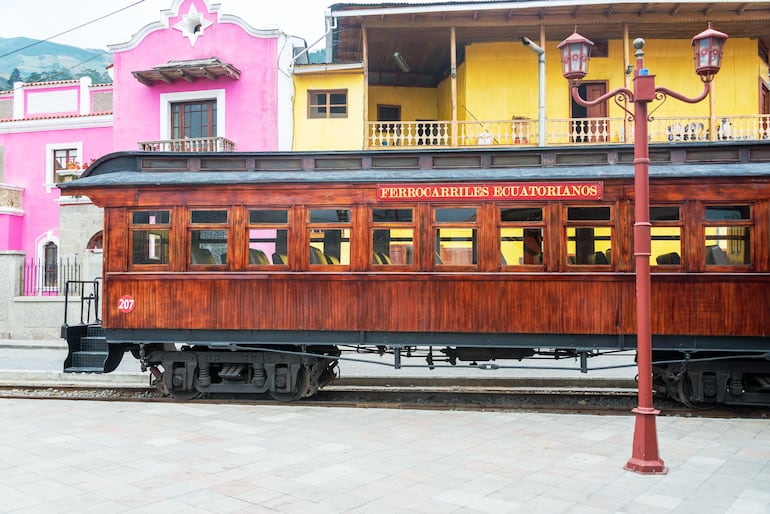 Vehículo ferroviario estacionado frente a coloridos edificios en la ciudad de Alausí, Ecuador.