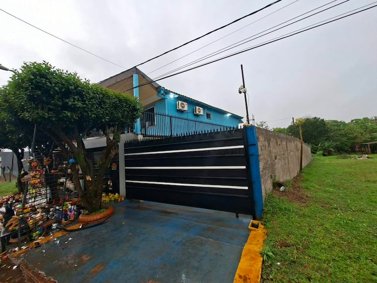 Propiedad con paredes azules y puerta negra, decoraciones en el acceso y árboles en el entorno verde.