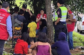 Grupo bajo un árbol con adultos en uniforme policial y chalecos rojos, varios niños, uno con camiseta amarilla de Neymar Jr.
