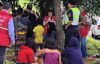 Grupo bajo un árbol con adultos en uniforme policial y chalecos rojos, varios niños, uno con camiseta amarilla de Neymar Jr.