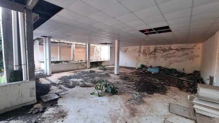 Interiores deteriorados del Palacete Municipal con piso de baldosas sueltas y paredes manchadas en un ambiente de abandono.