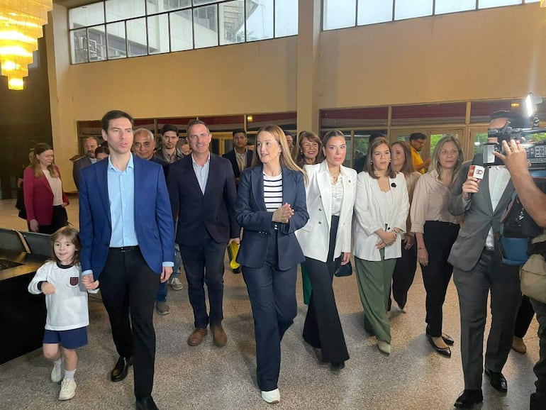Soledad Núñez en chaqueta oscura y camisa a rayas sonríe junto a su equipo en ambiente iluminado con ventanas grandes.