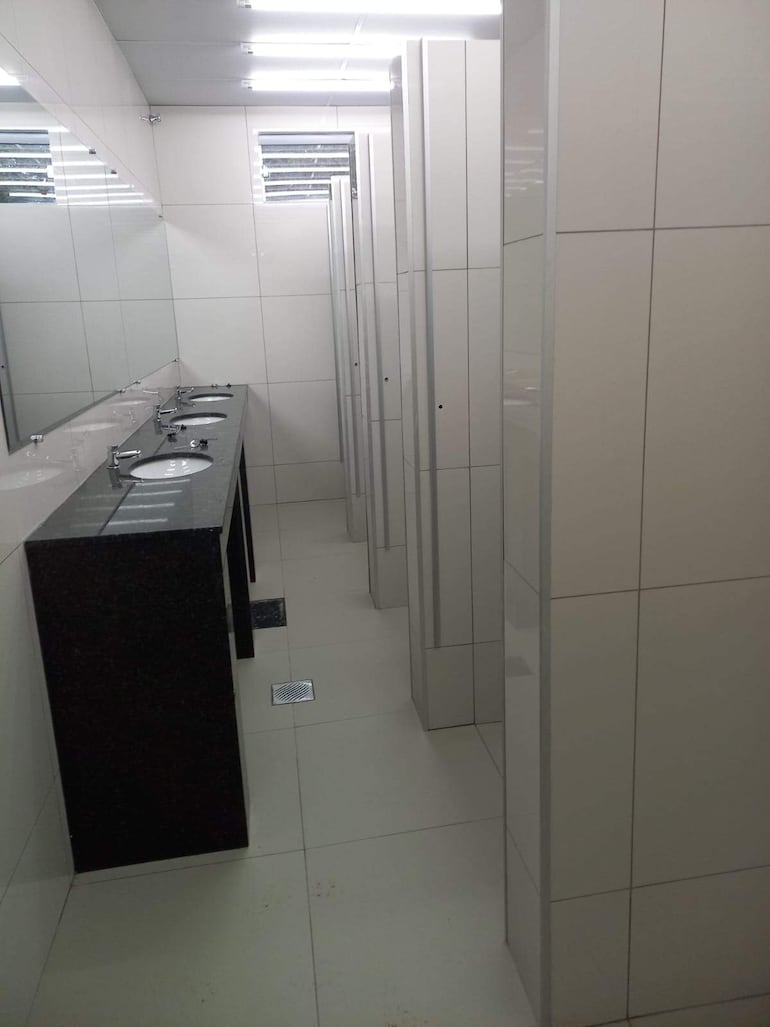 Baño interior moderno y luminoso, con filas de lavamanos y espejos en un ambiente limpio y funcional.