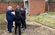 Héctor Daniel Granada en traje azul sostiene documentos, mientras otros participan en la conversación, rodeados de un área verde descuidada.