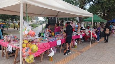 Vendedores en la feria con mesas decoradas, algunas personas observan productos variados en un ambiente relajado.