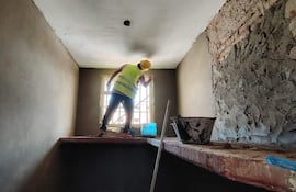 Hombre en chaleco reflectante amarillo y casco trabaja en la pared de una habitación en remodelación.