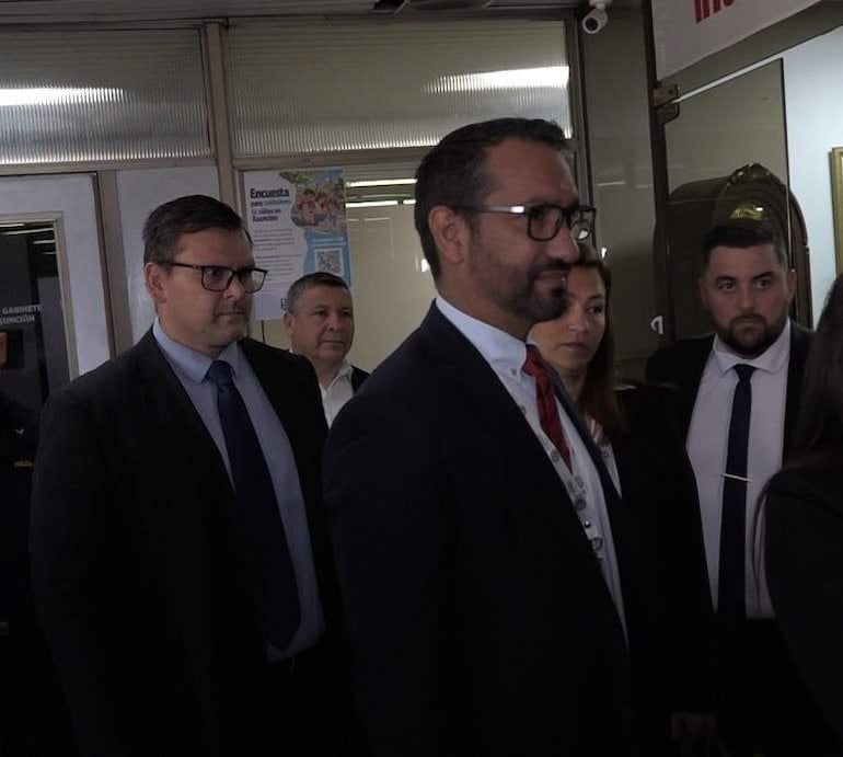 Grupo de seis personas en ambiente formal, tres hombres y tres mujeres con trajes oscuros y blusas claras, interactuando entre sí.