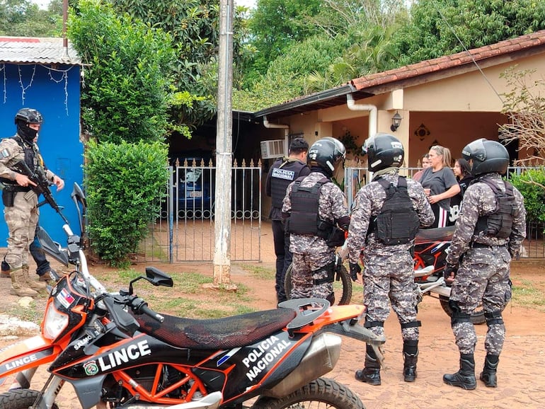 Cuatro agentes de la Policía Nacional interactúan con una mujer en un operativo, rodeados de motocicletas y ambiente suburbano.