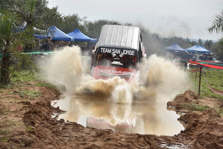 Vehículo del Team San Jorge genera salpicaduras al atravesar un charco en competencia off-road, con carpas azules de fondo.