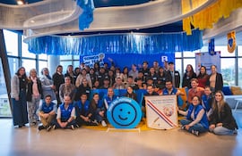 Grupo de estudiantes y adultos sonrientes en camisetas azules sosteniendo un banner, bajo un letrero de Tour del Futuro.