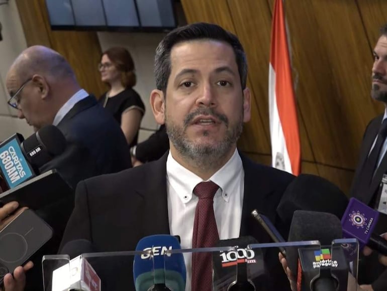 Raúl Latorre en traje negro y corbata roja, hablando ante un grupo de personas en un auditorio con micrófonos.