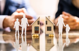 Figuras en miniatura representan a una familia en conflicto sobre bienes mientras abogados discuten documentos en la mesa.