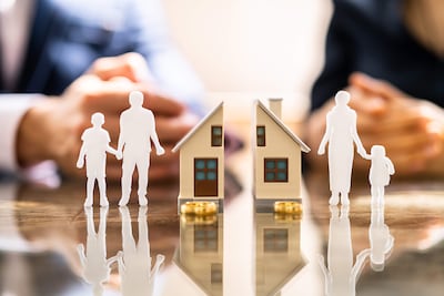 Figuras en miniatura representan a una familia en conflicto sobre bienes mientras abogados discuten documentos en la mesa.