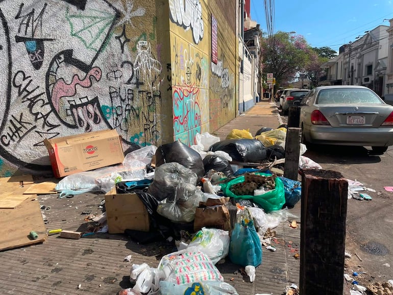 Montón de basura en acera con graffitis coloridos de fondo, sin personas visibles.