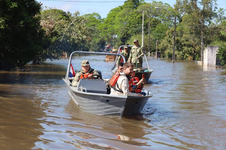 Tres hombres en botes de rescate, uno con gorro militar, otro con dispositivo móvil y otro con chaleco salvavidas, todo en un entorno inundado.