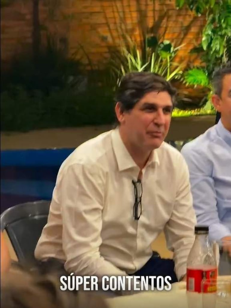 Raúl Codas Morselli, con camisa blanca, escucha atentamente a un hombre con camisa azul en un ambiente cálido y acogedor.