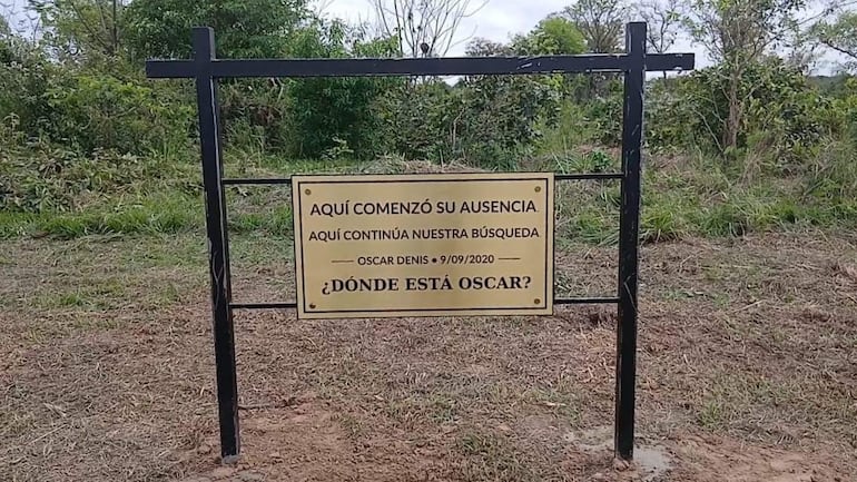 Cartel dorado con mensaje sobre la búsqueda de Oscar Denis en un área natural sin presencia de personas.
