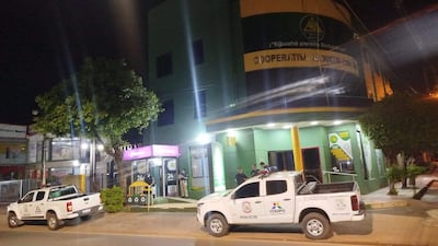 Tres oficiales de policía en frente de la Cooperativa Reducto, vigilando la escena con vehículos patrulleros visibles detrás.