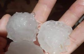 Tres bolas de granizo de diferentes tamaños y formas, con superficie irregular y brillante, sosteniéndose en una mano. Alrededor, un ambiente oscuro.