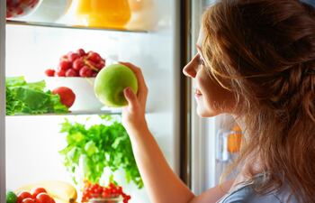 Mujer toma una manzana de la heladera.