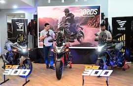 Hombre con camiseta de Voge habla frente a dos motocicletas DS300 en un salón moderno y bien iluminado.