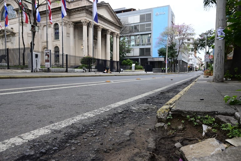 Calle semi-desierta con pavimento dañado y un edificio monumental con columnas en el fondo.