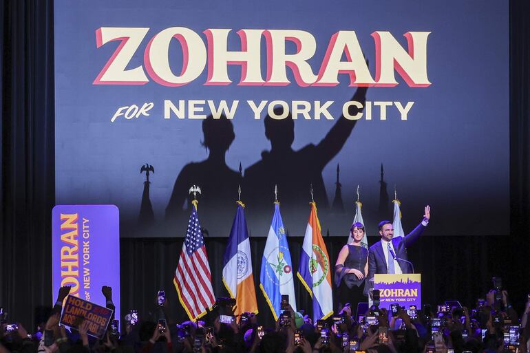 El alcalde electo de la ciudad de Nueva York, Zohran Mamdani (i), y su esposa, Rama Duwaji (d), saludan a la multitud durante una fiesta celebrada por el candidato demócrata en Brooklyn, Nueva York.