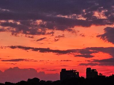 Cielo nublado con fondo de colores anaranjados y rosados, sobre dos edificios de altura a la distancia.