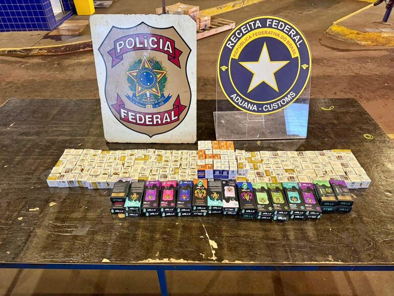 Mesa con paquetes de productos confiscados, carteles de Policía Federal y Receita Federal al fondo.