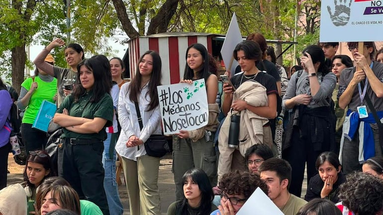 Mujer en el centro sostiene un cartel '#Los Médanos Nosetocan', rodeada de jóvenes con camisetas de colores en un ambiente de protesta.