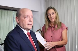 César Diesel con suit oscuro y corbata roja, Ingrid Junghanns en blusa rosa sosteniendo un documento en ambiente de oficina.