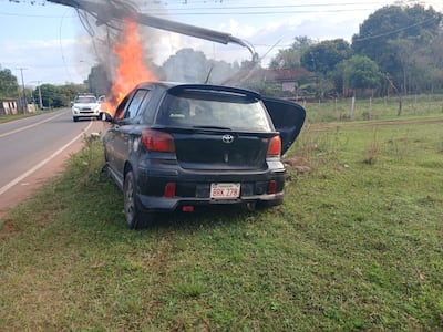 El automovil está siendo consumido por las llamas luego de chocar de frente contra una columna sobre la Ruta Departamental D023, en la jurisdicción de Paraguarí.