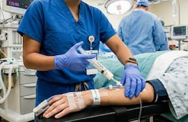 Profesionales de la salud en camiseta azul y guantes azules, administrando tratamiento a paciente con vendaje en el brazo.