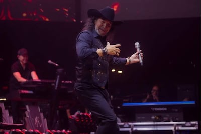 Cantante con sombrero negro y camisa oscura brilla en el escenario, sosteniendo un micrófono y disfrutando el momento.