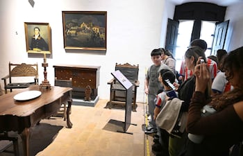 Grupo de niños, liderado por uno de camiseta gris, observan pinturas en un ambiente luminoso de museo.