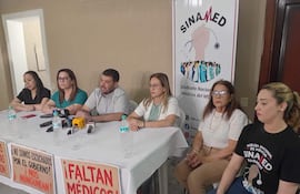 Dra. Sandra Prantte y Dr. Roberto Riveros en conferencia de prensa, rodeados de colegas, todos expresando seriedad y determinación.