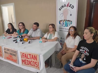 Dra. Sandra Prantte y Dr. Roberto Riveros en conferencia de prensa, rodeados de colegas, todos expresando seriedad y determinación.