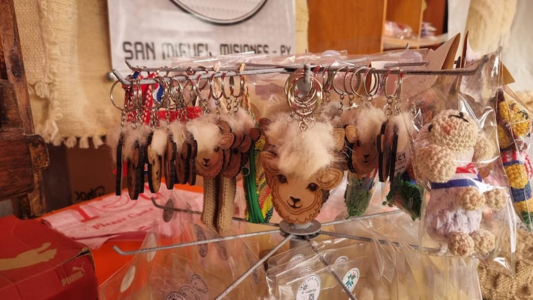 Exhibidor giratorio con llaveros de ovejas estilizadas, varios colores, ambiente acogedor de mercado.