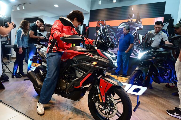 Motocicleta Voge de color negro y rojo con un hombre de cabello rizado en atuendo rojo sentado sobre ella, rodeado de otros asistentes.