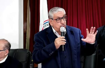 Isaías Ricardo Fretes, con chaqueta azul y gafas, habla con un micrófono, gesticulando ante una multitud en un auditorio.