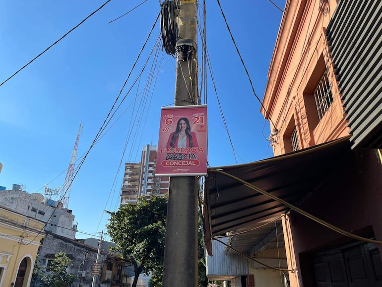 Cartel electoral de Florencia García con chaqueta blanca adherido a un poste en un ambiente urbano.