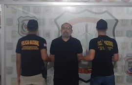 Tres hombres en oficina de seguridad, dos de espaldas con camisetas negras de Policía Nacional y uno al centro con gafas y barba.