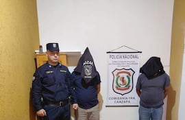Policía en uniforme y dos hombres con capuchas, rodeados de billetes paraguayos y documentos sobre una mesa.