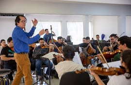 Diego Sánchez Haase dirige a músicos con instrumentos como violines en un ambiente luminoso y concentrado durante el ensayo.