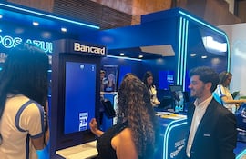 Mujer de cabello largo y lacio con camiseta clara sonríe frente a una pantalla. Ambiente azul y blanco, elementos promocionales de Bancard.