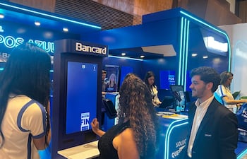 Mujer de cabello largo y lacio con camiseta clara sonríe frente a una pantalla. Ambiente azul y blanco, elementos promocionales de Bancard.