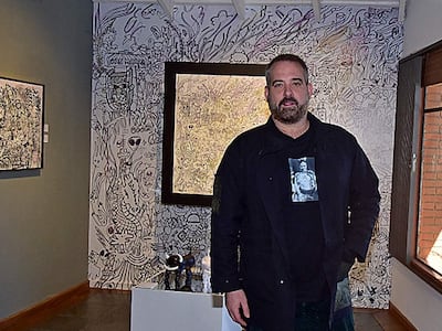 Hombre de mediana edad, con barba y abrigo oscuro, contempla obras en una galería decorada con arte abstracto.