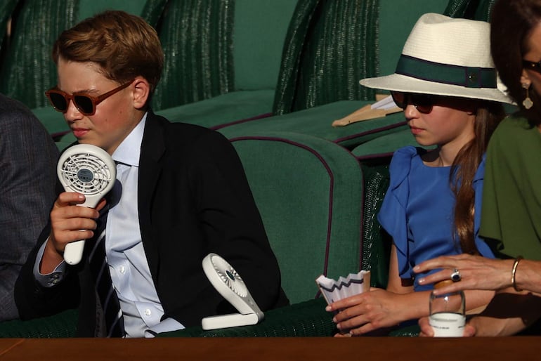 Los principitos George y Charlotte utilizaron pequeños ventiladores para refrescarse mientras presenciaban la final masculina individual de tenis, en la decimocuarta jornada del Campeonato de Wimbledon 2026, en el All England Lawn Tennis and Croquet Club. (Adrian Dennis / AFP)