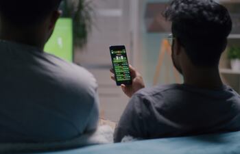 hinchas de futbol miran un partido en el televisor y en su celular