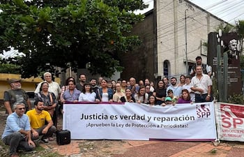 Grupo de personas sosteniendo un banner, algunos con expresiones de tristeza y alegría en un acto de protesta en un espacio urbano.